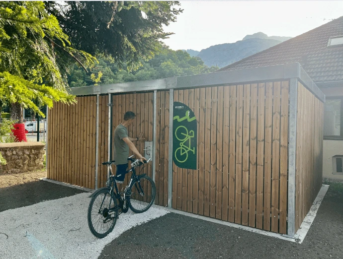 Abri vélo bois sécurisé Bycommute avec un cycliste accédant au système de verrouillage, installé en extérieur près d’un bâtiment, en zone montagneuse.