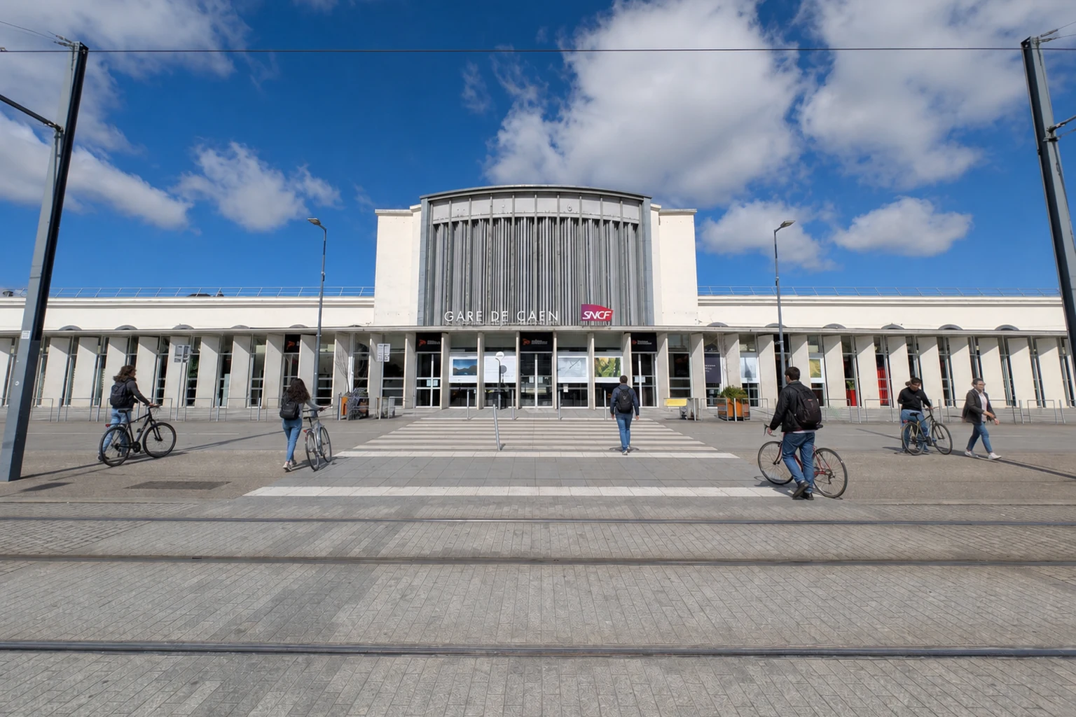 Autre cadrage de la gare réelle de Caen avec des voyageurs marchant à côté de leur vélo