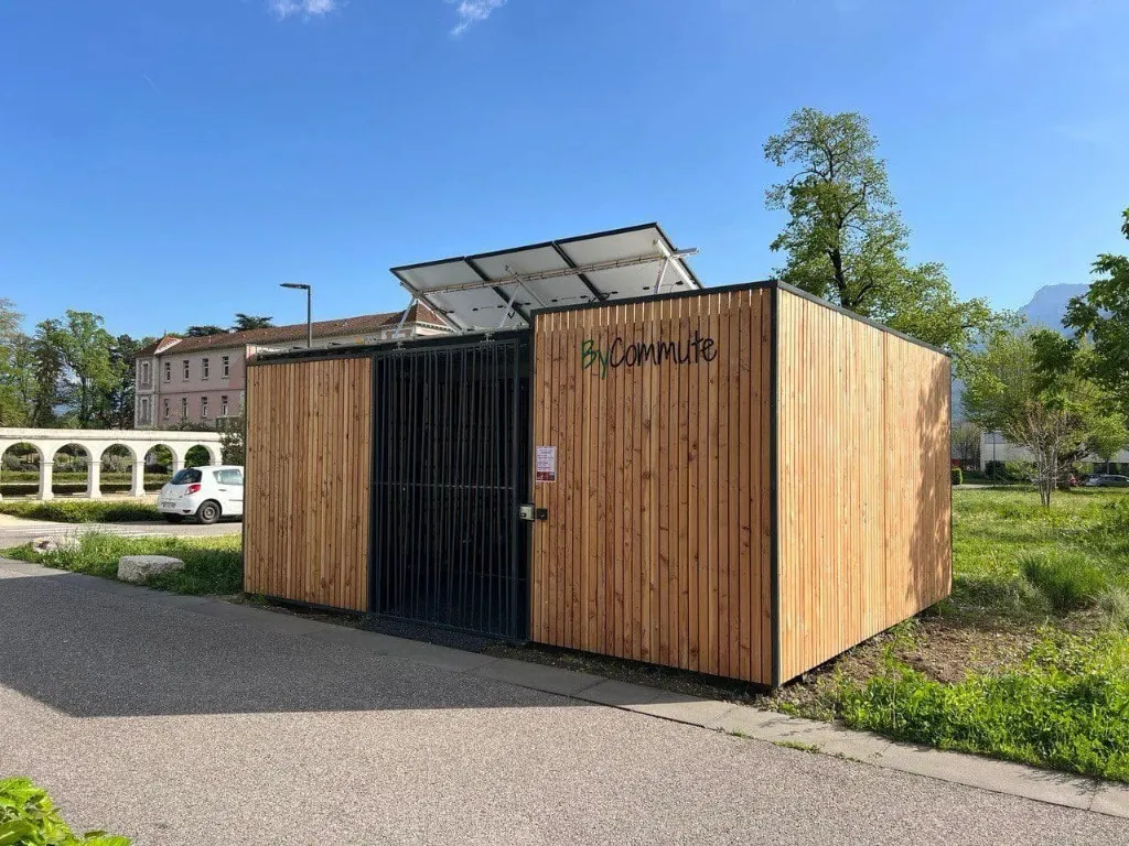 Abri vélo ByCommute en bois, fermé par une grille, avec panneaux photovoltaïques inclinés en toiture